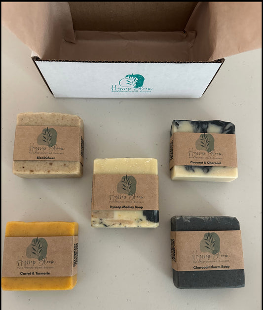 Five bars of soap with cardboard wraps on a white surface, with a box in the background.